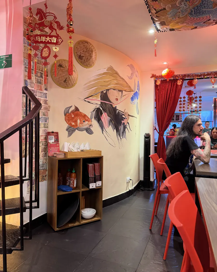 Interior de District 1 con mural de una mujer vietnamita, faroles rojos y sillas rojas
